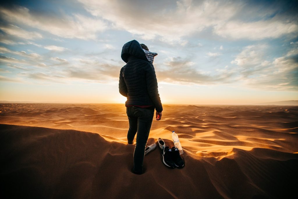 man in black jacket and gray pants standing on brown sand during daytime